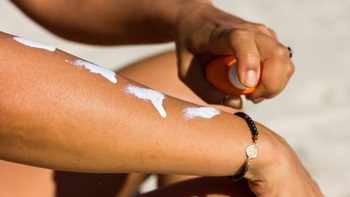 close-up van iemand die zonnecreme op arm spuit